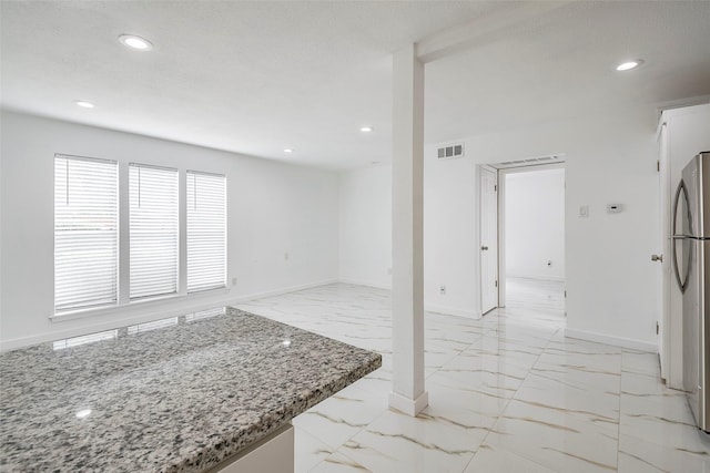 interior space featuring visible vents, baseboards, marble finish floor, freestanding refrigerator, and light stone countertops