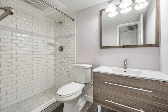 bathroom with toilet, vanity, a tile shower, and a textured wall