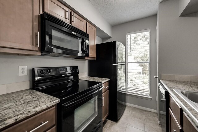 kitchen featuring light tile patterned floors, baseboards, a textured ceiling, black appliances, and a sink