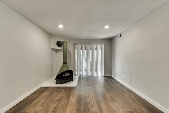 unfurnished living room featuring a wood stove, baseboards, visible vents, and wood finished floors