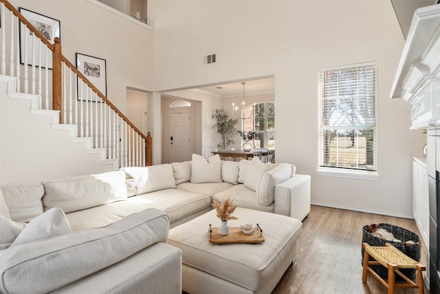 living room featuring wood finished floors, visible vents, a high ceiling, a fireplace, and stairs