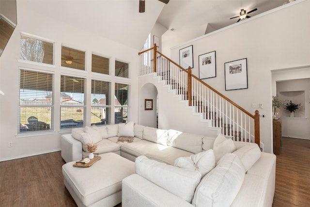 living room featuring stairway, dark wood-style floors, baseboards, high vaulted ceiling, and ceiling fan