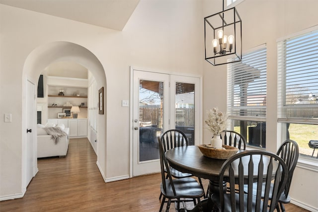 dining space featuring built in features, wood finished floors, a towering ceiling, arched walkways, and a chandelier