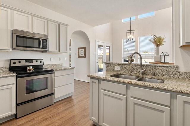 kitchen featuring light wood finished floors, light stone countertops, arched walkways, stainless steel appliances, and a sink