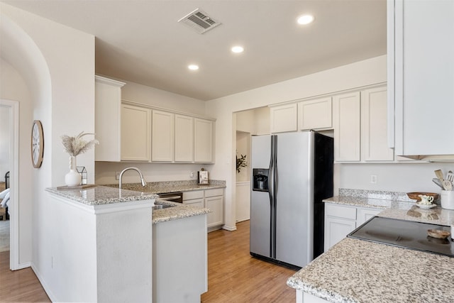 kitchen with light stone countertops, visible vents, light wood finished floors, a peninsula, and stainless steel fridge