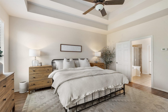 bedroom with a tray ceiling, baseboards, ensuite bath, and wood finished floors