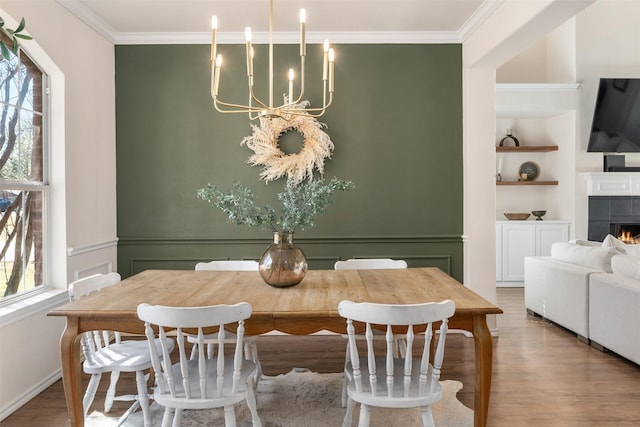 dining room with built in shelves, wood finished floors, a fireplace, crown molding, and a chandelier