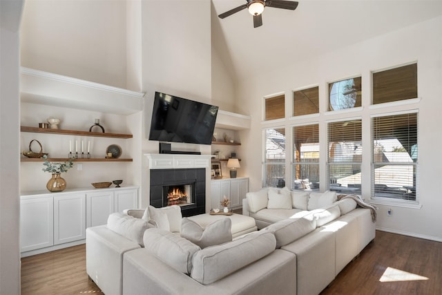 living area with a tile fireplace, high vaulted ceiling, built in shelves, and wood finished floors