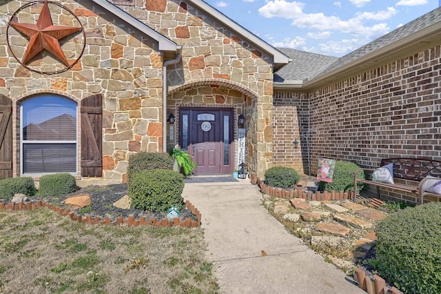 view of exterior entry featuring stone siding, brick siding, and roof with shingles