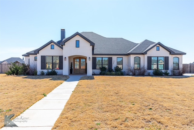 view of front of home with a shingled roof, a chimney, fence, french doors, and a front lawn