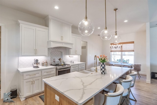 kitchen featuring a kitchen island with sink, a sink, white cabinets, decorative backsplash, and stainless steel gas stove