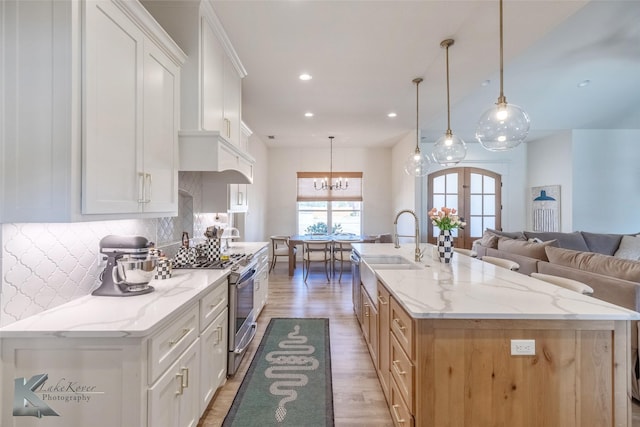 kitchen featuring light wood-style flooring, decorative backsplash, open floor plan, a large island with sink, and stainless steel gas range oven