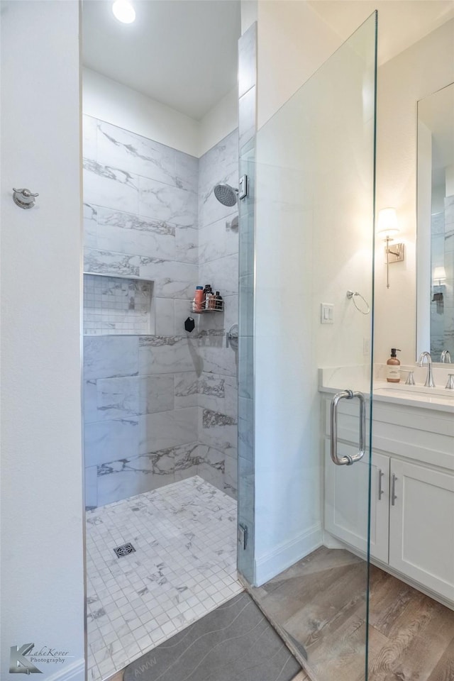 full bath featuring wood finished floors, a shower stall, vanity, and baseboards