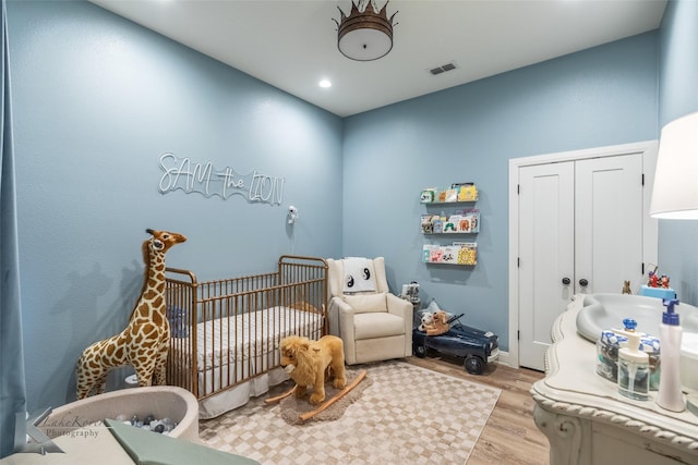 bedroom featuring a crib, visible vents, wood finished floors, a closet, and recessed lighting