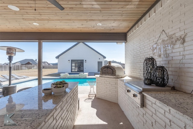 view of patio with exterior kitchen, an outdoor structure, fence, and a pool with connected hot tub