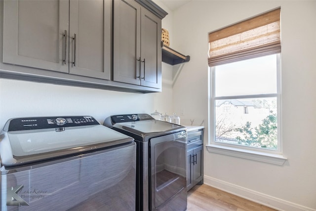 washroom with cabinet space, washing machine and dryer, baseboards, and light wood-style floors