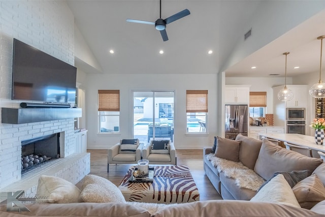 living room featuring a fireplace, light wood finished floors, recessed lighting, ceiling fan, and high vaulted ceiling