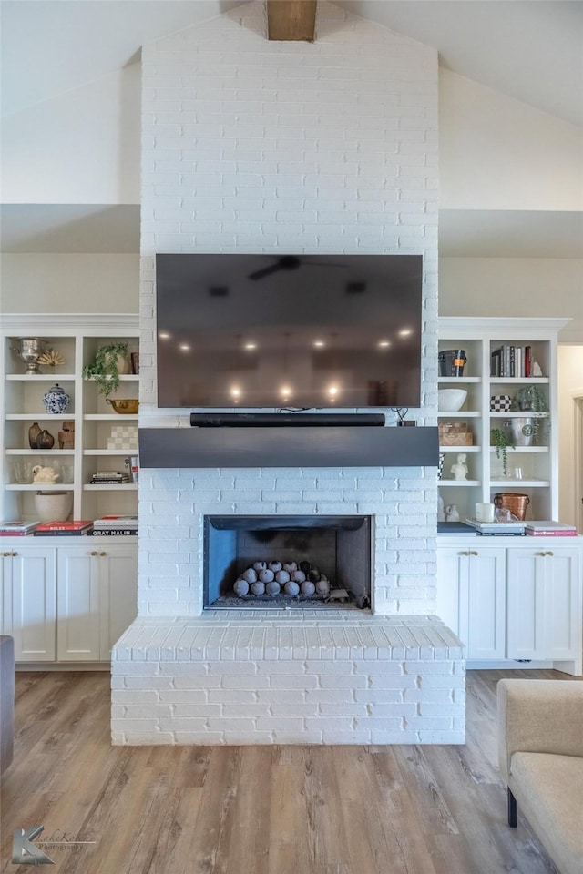 unfurnished living room with lofted ceiling, a brick fireplace, and light wood-style flooring