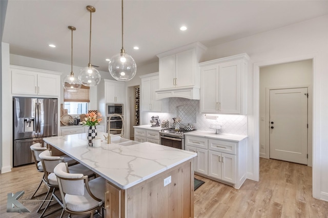 kitchen featuring white cabinets, premium range hood, a kitchen island with sink, and stainless steel appliances