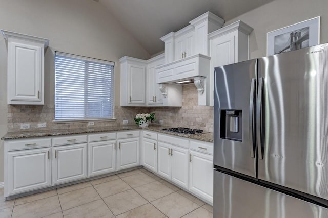 kitchen with appliances with stainless steel finishes, white cabinetry, vaulted ceiling, light tile patterned flooring, and light stone countertops