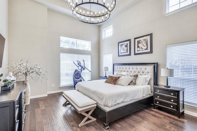 bedroom featuring an inviting chandelier, a high ceiling, baseboards, and dark wood-type flooring