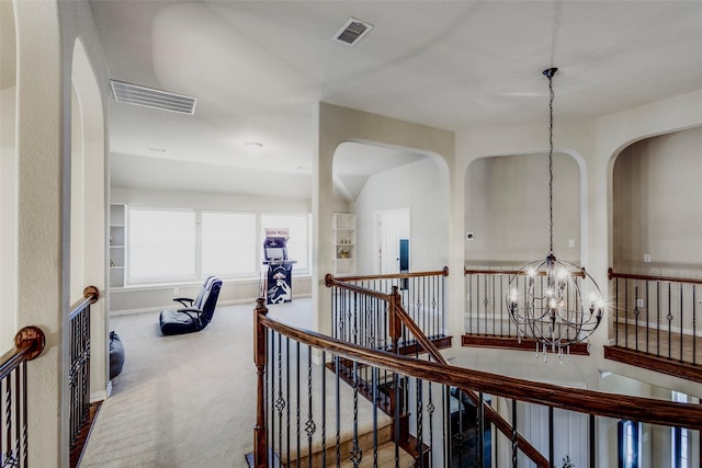 hall with visible vents, carpet, an upstairs landing, and an inviting chandelier