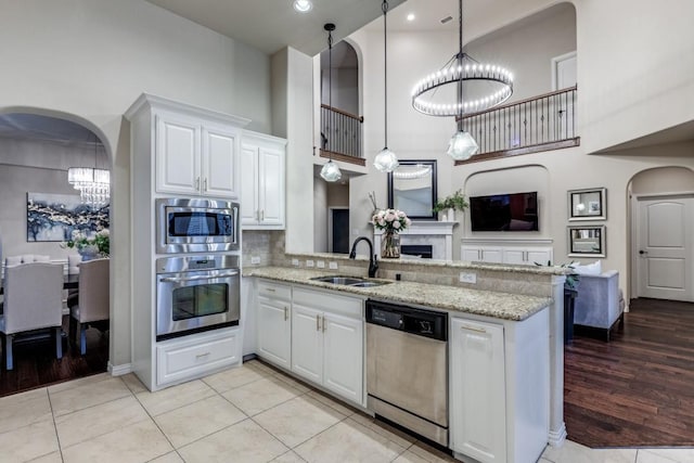 kitchen featuring arched walkways, a peninsula, appliances with stainless steel finishes, and a sink