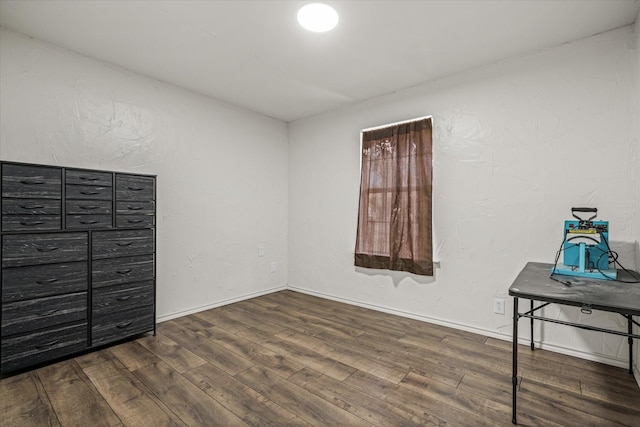 empty room with baseboards, wood finished floors, and a textured wall