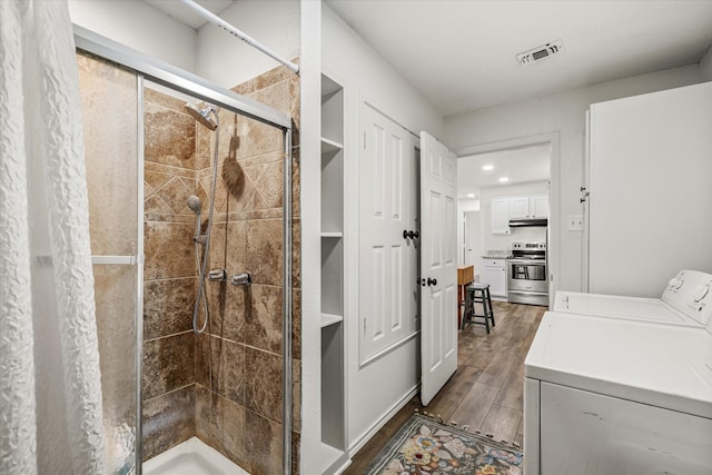 bathroom with a stall shower, wood finish floors, washing machine and dryer, and visible vents