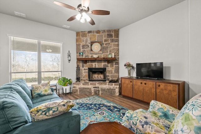 living room with a ceiling fan, visible vents, a stone fireplace, and wood finished floors