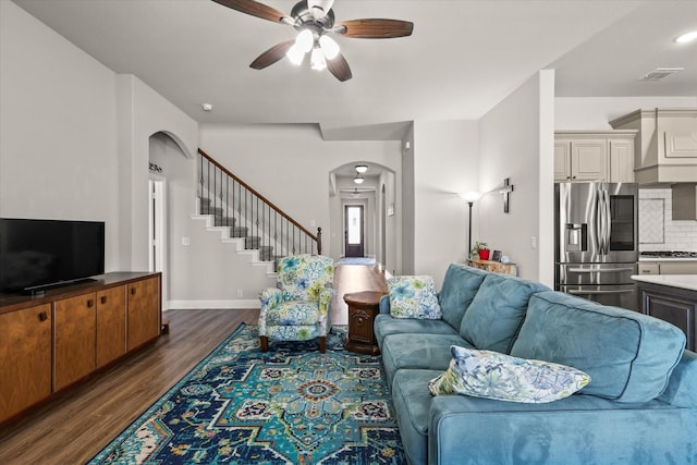 living room featuring arched walkways, dark wood-style flooring, a ceiling fan, baseboards, and stairs