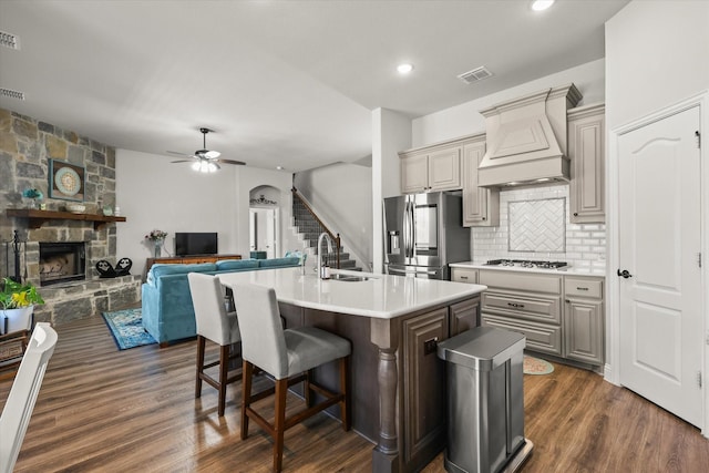 kitchen with a breakfast bar, a fireplace, custom range hood, a sink, and stainless steel fridge