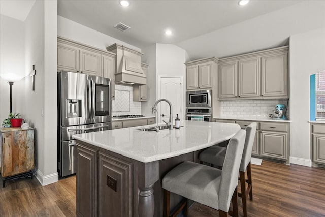 kitchen featuring visible vents, dark wood-type flooring, stainless steel appliances, premium range hood, and a sink