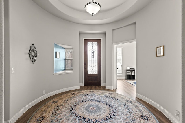 entryway featuring a tray ceiling, baseboards, and dark wood-type flooring