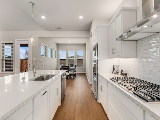 kitchen featuring light wood finished floors, light countertops, appliances with stainless steel finishes, wall chimney exhaust hood, and a sink