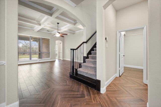 staircase featuring beam ceiling, coffered ceiling, arched walkways, baseboards, and ceiling fan