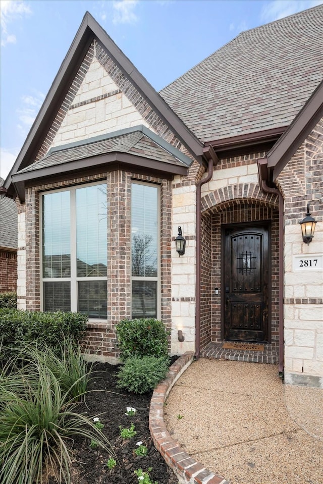 entrance to property featuring brick siding and roof with shingles