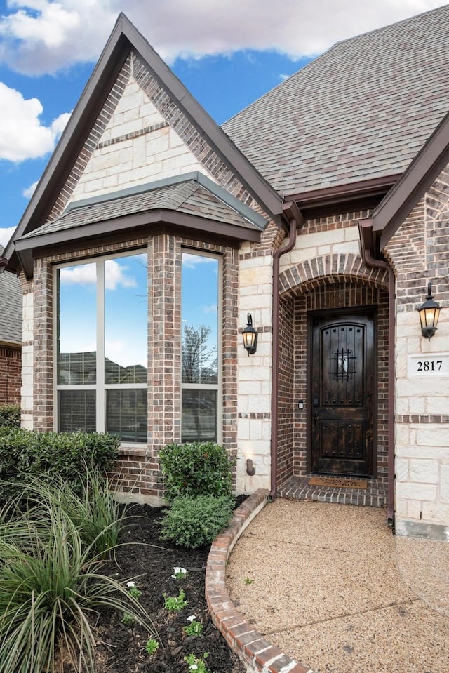 entrance to property featuring brick siding and a shingled roof