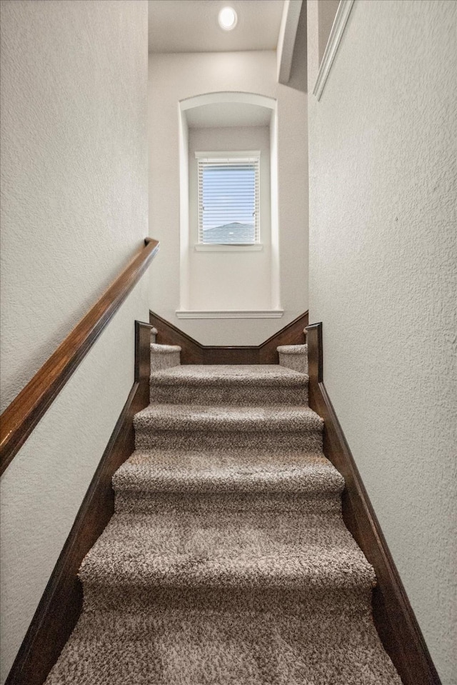 stairs featuring a textured wall, baseboards, and arched walkways