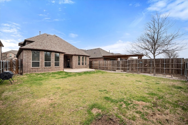 rear view of house featuring brick siding, a shingled roof, a lawn, a fenced backyard, and a patio area