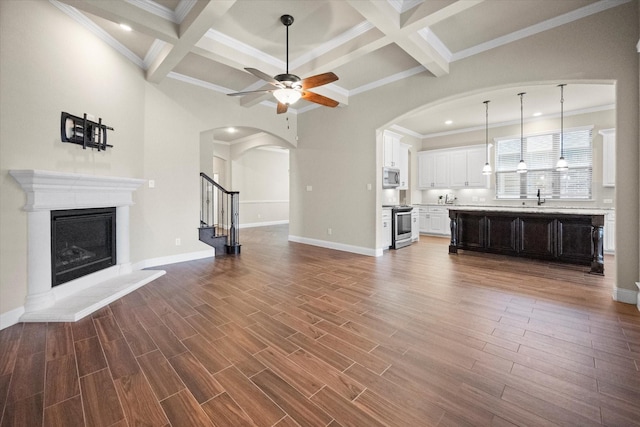 unfurnished living room featuring dark wood finished floors, a fireplace with raised hearth, arched walkways, and a ceiling fan