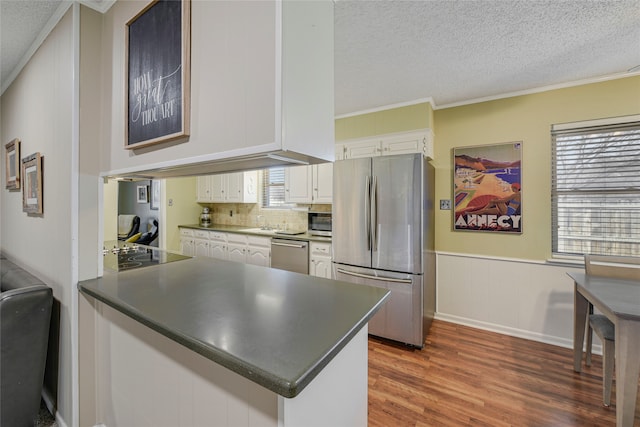 kitchen with dark countertops, appliances with stainless steel finishes, white cabinets, wainscoting, and wood finished floors