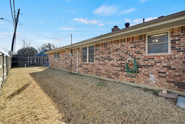 view of side of property featuring brick siding, fence, a chimney, and a lawn