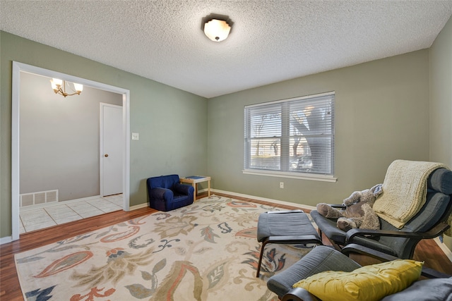 living area featuring visible vents, a textured ceiling, wood finished floors, a chandelier, and baseboards