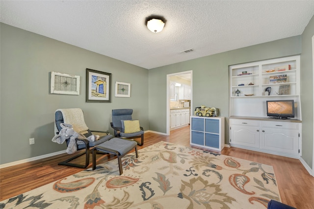 sitting room featuring a textured ceiling, light wood-style flooring, visible vents, and baseboards