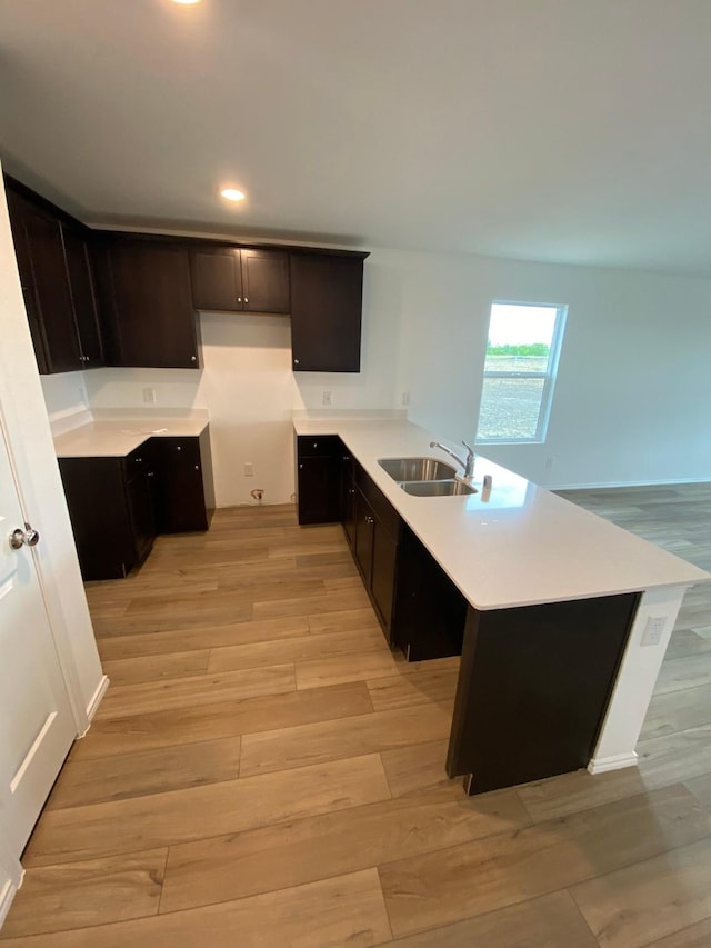 kitchen with recessed lighting, light wood-style floors, a sink, dark brown cabinets, and a peninsula