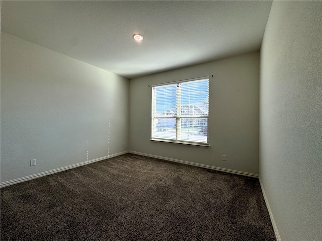 spare room with dark colored carpet and baseboards