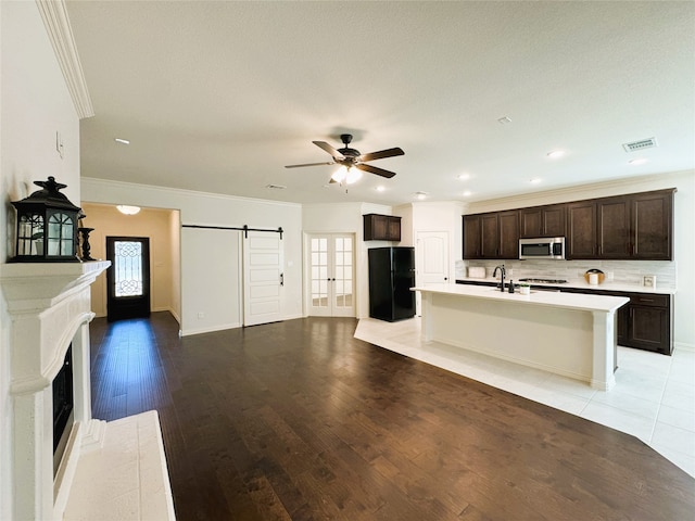 kitchen featuring dark brown cabinetry, a barn door, stainless steel microwave, freestanding refrigerator, and a sink