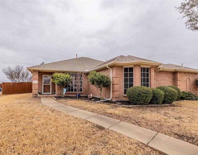 single story home featuring a shingled roof, brick siding, and fence