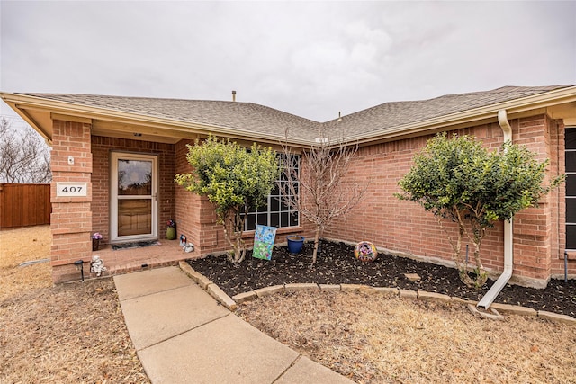 property entrance with brick siding, a shingled roof, and fence